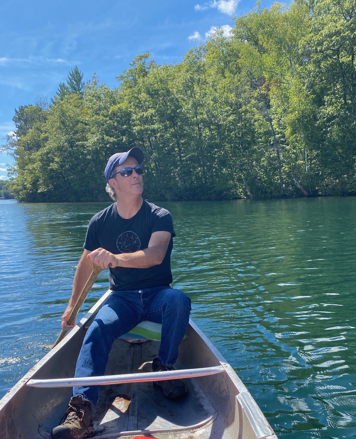 A man sits in a canoe on a lake holding a paddle